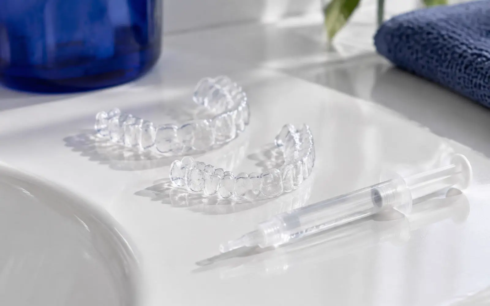 Twee doorzichtige bleeklepels en een spuitje met heldere gel op een wit vlak
