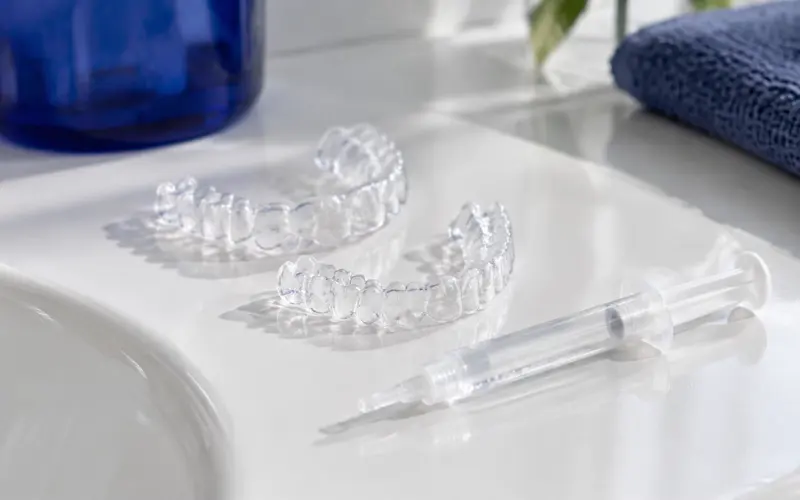 Twee doorzichtige bleeklepels en een spuitje met heldere gel op een wit vlak